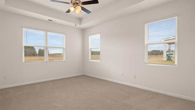 spare room featuring ceiling fan, carpet floors, visible vents, baseboards, and a tray ceiling