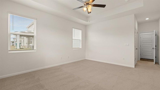 spare room featuring a raised ceiling, light carpet, ceiling fan, and baseboards