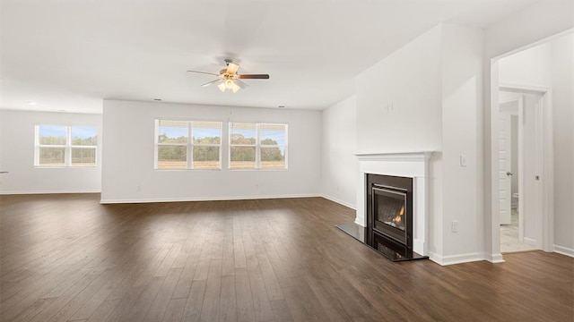 unfurnished living room featuring dark wood-type flooring, a glass covered fireplace, ceiling fan, and baseboards