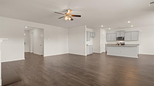 unfurnished living room featuring baseboards, ceiling fan, visible vents, and dark wood-style flooring