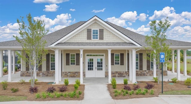 view of front of property with covered porch, stone siding, french doors, and roof with shingles