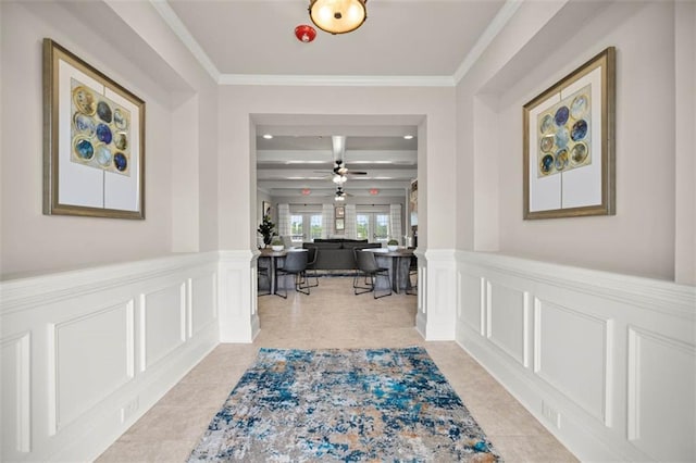 corridor with light tile patterned floors, a decorative wall, crown molding, and a wainscoted wall