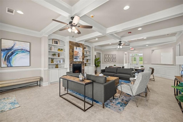 living area with visible vents, beamed ceiling, a stone fireplace, built in shelves, and a decorative wall