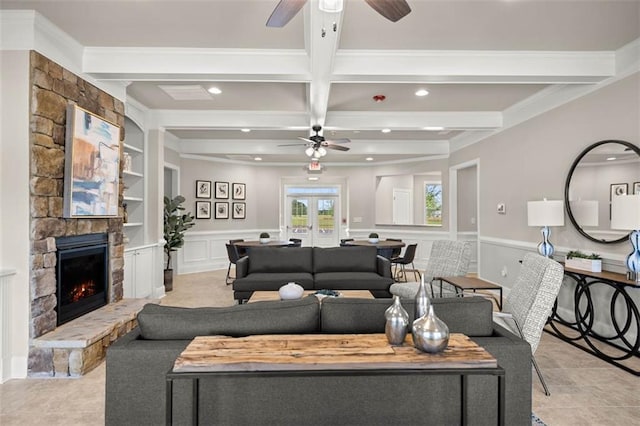 living area featuring a wainscoted wall, built in shelves, beam ceiling, and a stone fireplace