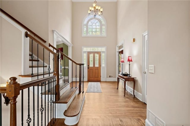 foyer entrance with visible vents, a notable chandelier, wood finished floors, baseboards, and a towering ceiling