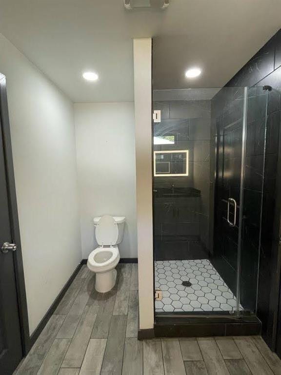 bathroom with a shower stall, toilet, wood tiled floor, and recessed lighting