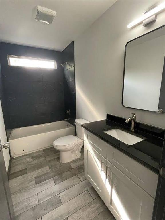 bathroom with toilet, vanity, wood finished floors, and  shower combination