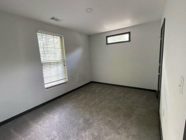 spare room featuring baseboards, visible vents, and dark carpet