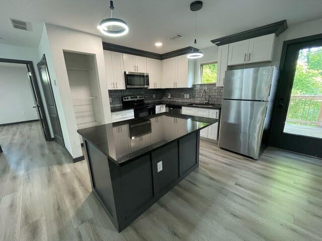 kitchen featuring dark countertops, a sink, stainless steel appliances, white cabinets, and visible vents