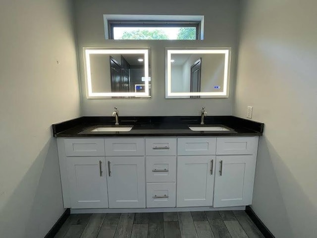 bathroom featuring baseboards, wood finished floors, a sink, and double vanity