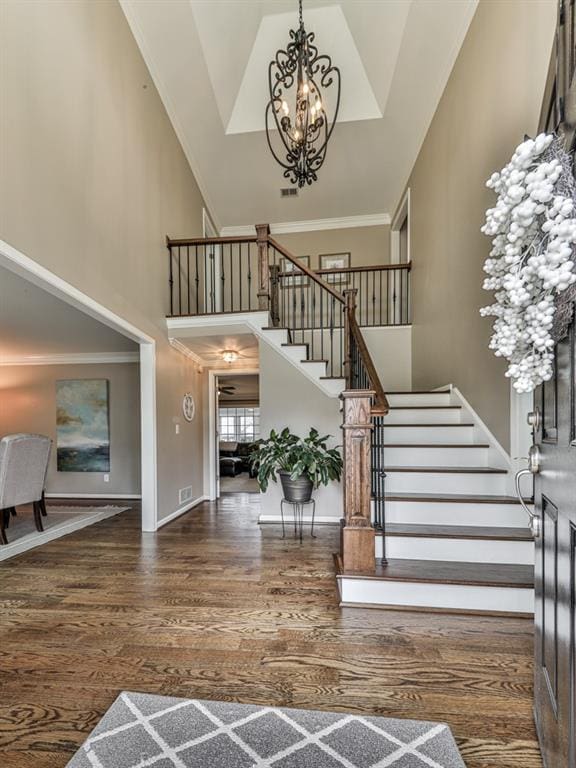 entrance foyer featuring a towering ceiling, dark hardwood / wood-style flooring, crown molding, and a notable chandelier