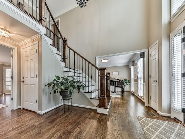 entryway with a towering ceiling, ornamental molding, and dark wood-type flooring