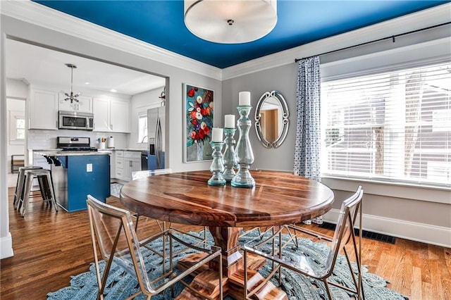 dining area with baseboards, wood finished floors, visible vents, and ornamental molding