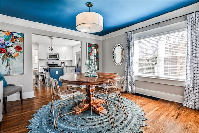 dining room with baseboards, wood finished floors, visible vents, and ornamental molding