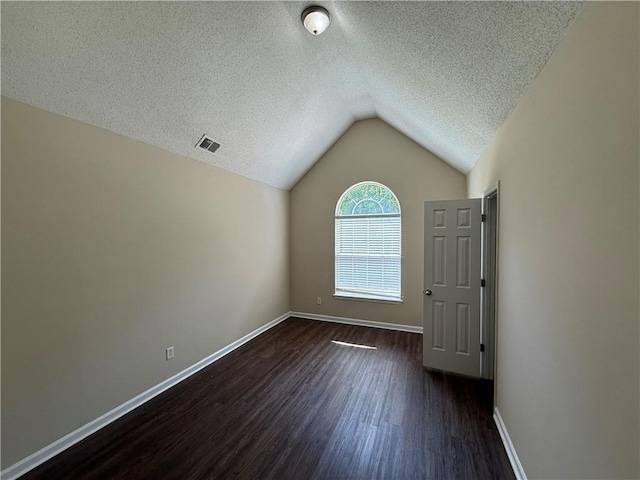 empty room with a textured ceiling, visible vents, vaulted ceiling, baseboards, and dark wood-style floors