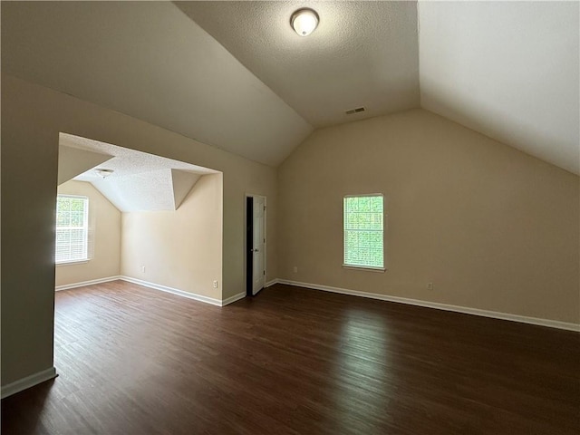 bonus room featuring a textured ceiling, vaulted ceiling, dark wood finished floors, and visible vents