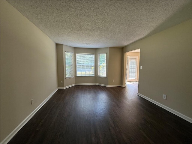 empty room with a textured ceiling, dark wood-style floors, and baseboards