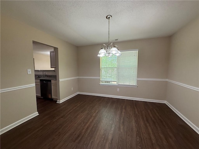 empty room with a textured ceiling, dark wood finished floors, a sink, baseboards, and a chandelier