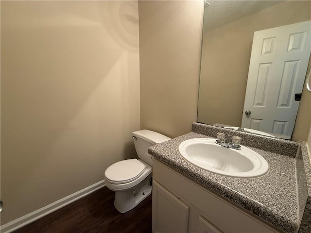 half bath featuring baseboards, wood finished floors, toilet, and vanity