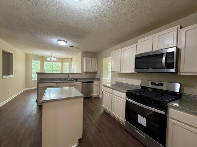 kitchen with a textured ceiling, appliances with stainless steel finishes, a sink, a peninsula, and dark wood-style floors