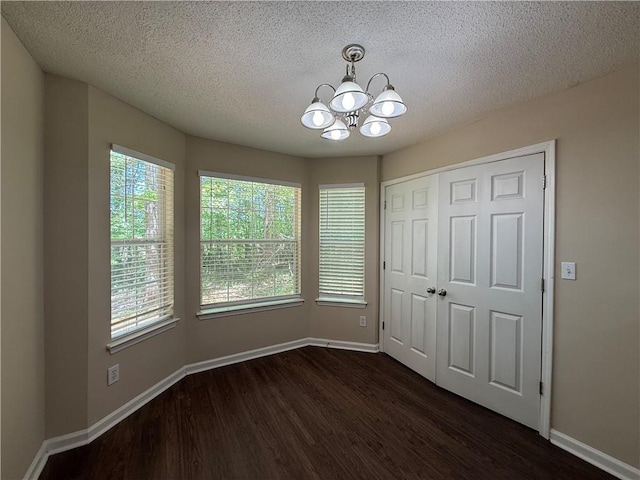 unfurnished dining area with an inviting chandelier, a textured ceiling, baseboards, and dark wood-type flooring