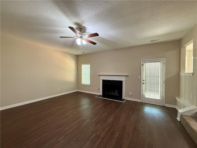 unfurnished living room with visible vents, dark wood-style flooring, a fireplace with raised hearth, a textured ceiling, and a ceiling fan