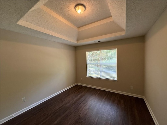 empty room featuring visible vents, baseboards, dark wood-style floors, a textured ceiling, and a raised ceiling