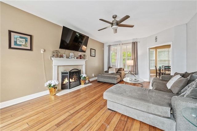 642 Towering Pine Trl, Lawrenceville, GA 30045 - living room featuring ceiling fan, light wood finished floors, a warm lit fireplace, and baseboards