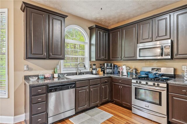 642 Towering Pine Trl, Lawrenceville, GA 30045 - kitchen with appliances with stainless steel finishes, a sink, light wood-style floors, dark countertops, and a textured ceiling