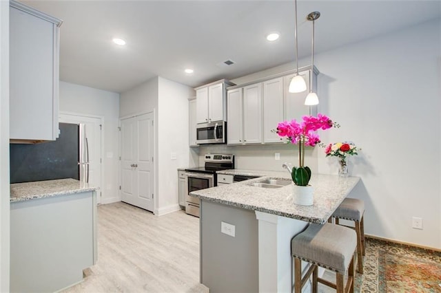 kitchen featuring light wood-style flooring, a breakfast bar, a peninsula, stainless steel appliances, and a sink