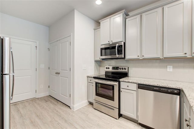 kitchen featuring stainless steel appliances, backsplash, light wood finished floors, and light stone countertops