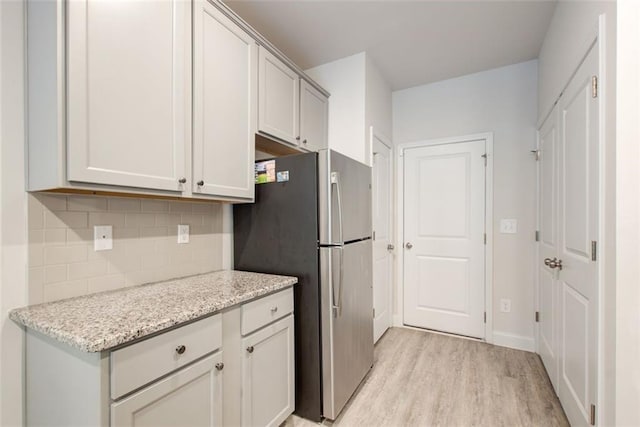 kitchen with light wood-style flooring, baseboards, freestanding refrigerator, light stone countertops, and tasteful backsplash