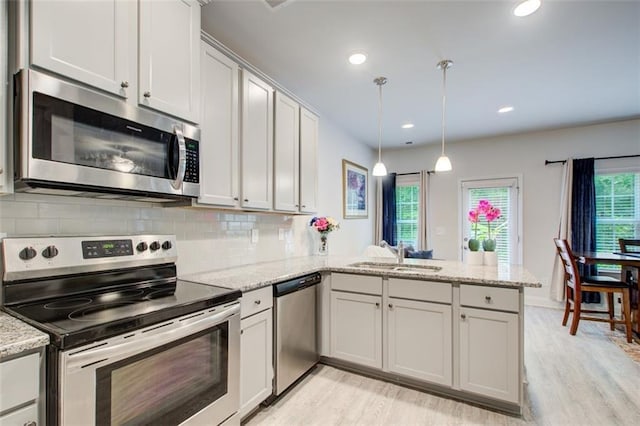 kitchen featuring light wood-style flooring, stainless steel appliances, a peninsula, a sink, and decorative backsplash