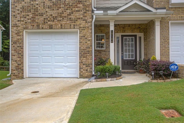 doorway to property featuring a garage, a yard, concrete driveway, and brick siding