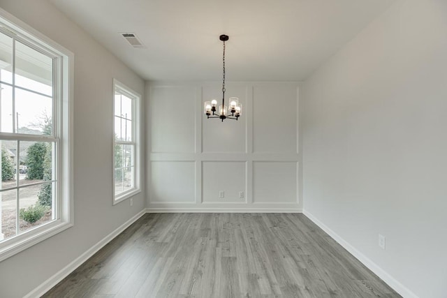 unfurnished dining area with an inviting chandelier, plenty of natural light, and hardwood / wood-style floors