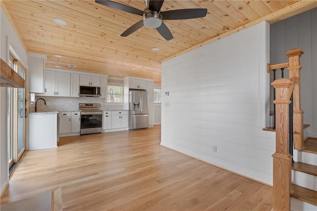 interior space with wood ceiling, a ceiling fan, white cabinetry, and stainless steel appliances
