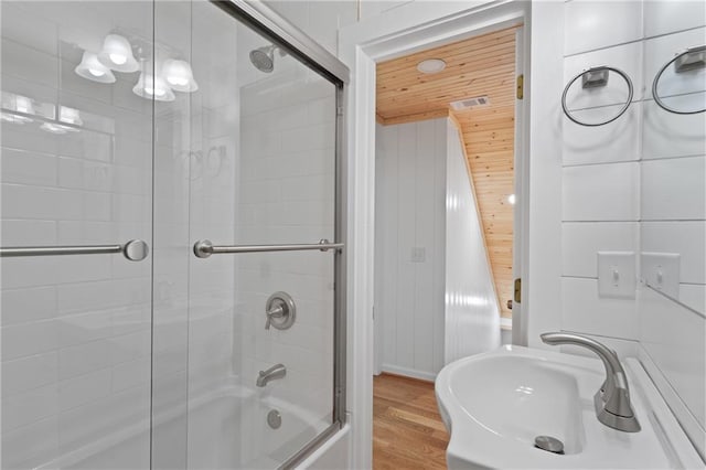 full bath featuring wood finished floors, wooden ceiling, enclosed tub / shower combo, and a sink