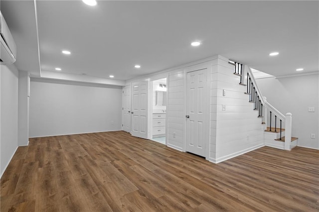 basement featuring recessed lighting, wood finished floors, an AC wall unit, and stairway