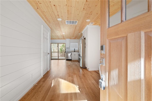 hall with a sink, light wood-style floors, wooden ceiling, wood walls, and visible vents