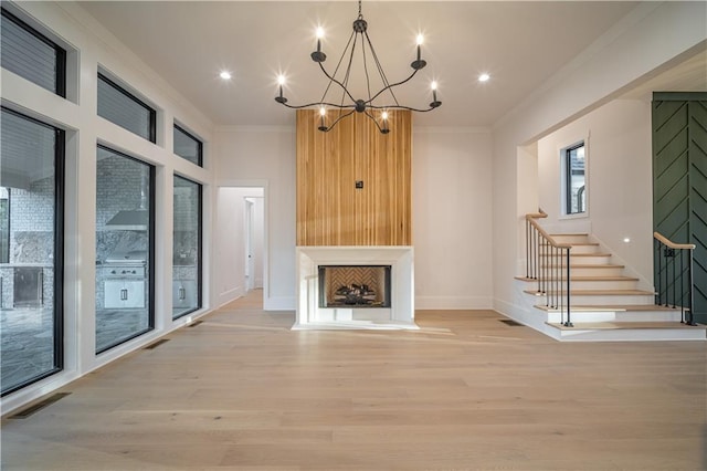 unfurnished living room featuring a chandelier, ornamental molding, a fireplace, and light hardwood / wood-style flooring