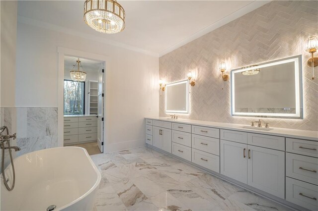 kitchen featuring an inviting chandelier, a center island with sink, sink, ornamental molding, and stone countertops