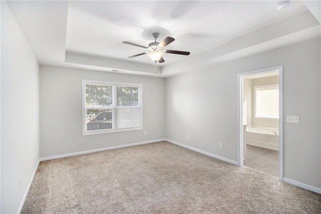 spare room with a healthy amount of sunlight, ceiling fan, light carpet, and a raised ceiling