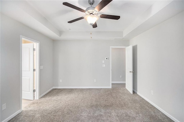 spare room featuring ceiling fan, light colored carpet, and a raised ceiling