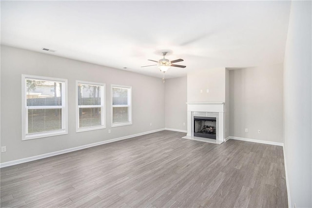 unfurnished living room with a high end fireplace, ceiling fan, and light hardwood / wood-style floors