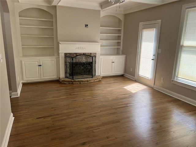 unfurnished living room featuring beamed ceiling, a healthy amount of sunlight, built in features, and a fireplace