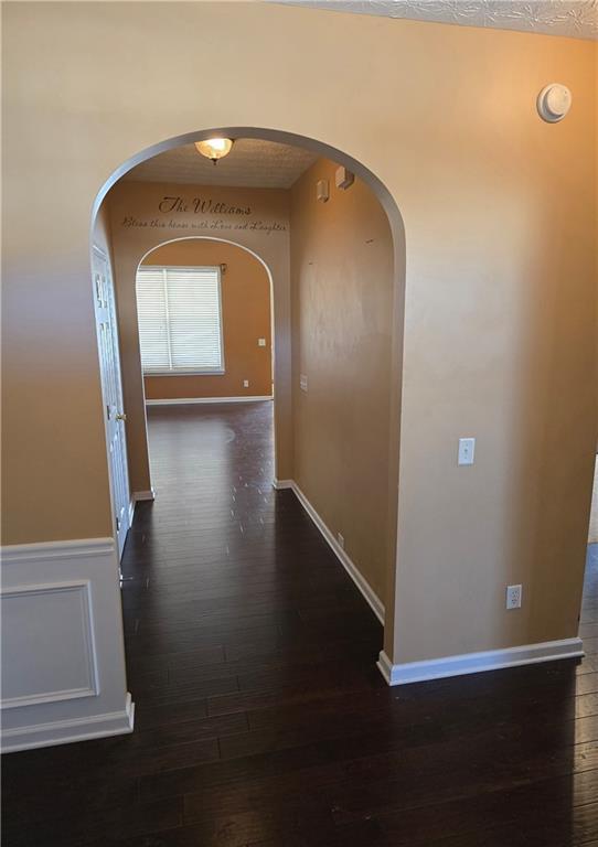 hallway with wood finished floors, arched walkways, and baseboards