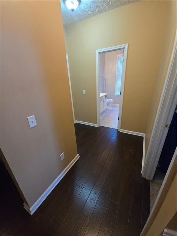 hall with dark wood-type flooring, baseboards, and a textured ceiling