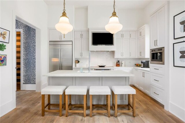 kitchen with light wood finished floors, backsplash, light countertops, appliances with stainless steel finishes, and a kitchen breakfast bar