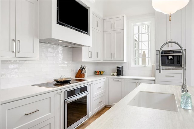 kitchen with oven, black electric stovetop, backsplash, and light countertops