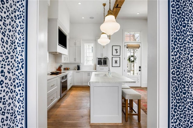 kitchen featuring a breakfast bar, black cooktop, light wood-style floors, light countertops, and stainless steel oven